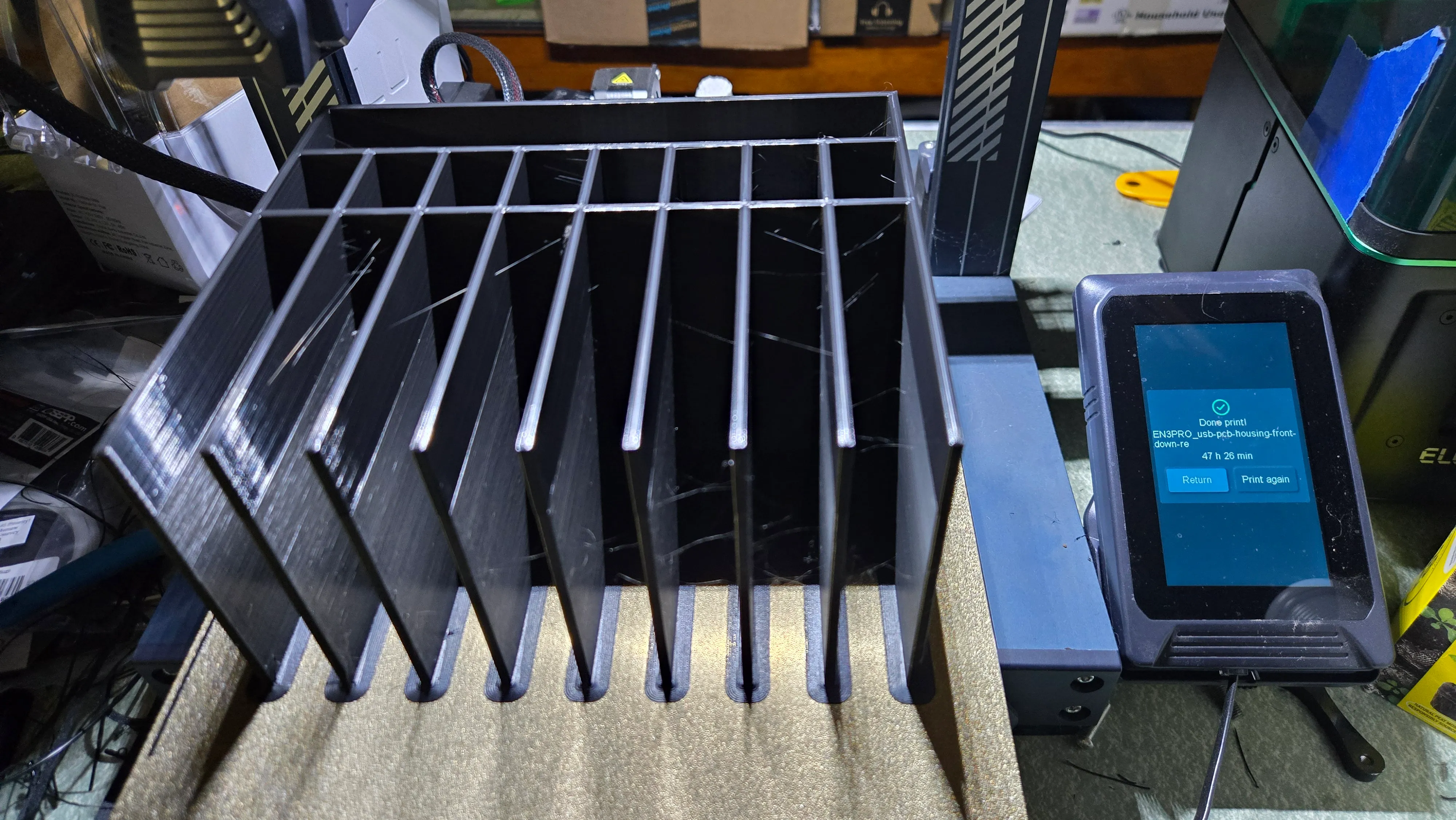 The freshly printed black enclosure, a grid of tall divider fins, sitting beside the printer's touchscreen reading "Done print!"